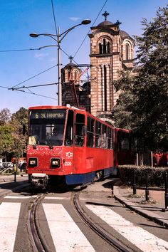 a red trolley is going down the tracks in front of an old church and clock tower