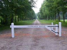 a white gate that is in the middle of a dirt road with trees on both sides