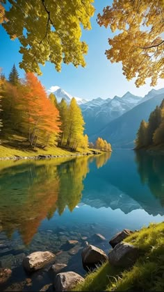 a lake surrounded by trees with mountains in the background and autumn foliage on the bank