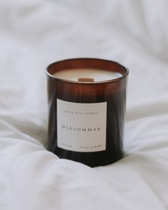 a candle sitting on top of a white bed next to a pillow with the label midsomar