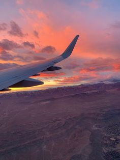 the wing of an airplane as it flies in the sky over mountains and land at sunset