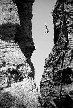 a person flying through the air while standing on top of a rock formation in front of a cliff