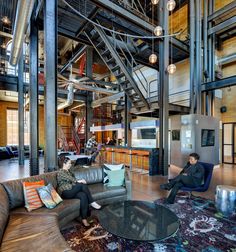 two people sitting on couches in a large room with high ceilings and exposed pipes