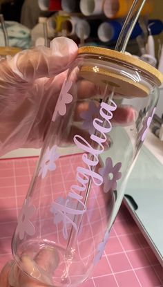 a person is holding a glass with the word hello kitty on it and pink flowers