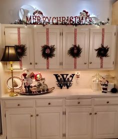 a kitchen with white cabinets and christmas decorations on the top shelf in front of it