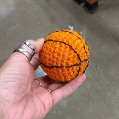 a hand holding an orange crocheted basketball ball in it's left hand