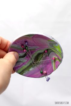 a hand holding a purple and green object with pins in it's back end