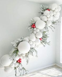 the balloon garland is decorated with white and red balls, greenery, and berries