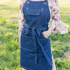 a woman standing in the grass wearing an overall dress with a tie around her waist