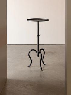 a black table sitting on top of a cement floor next to a white wall in an empty room