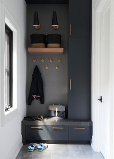 an entryway with black cabinets and gold handles on the doors, two coats hanging from hooks