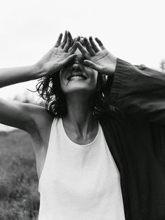 a black and white photo of a woman holding her hands up to her face while standing in a field