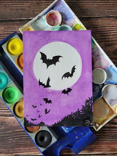 a purple card with bats on it sitting next to some paint and watercolors