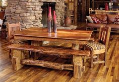 a wooden table and bench in a room with wood flooring, stone fireplace and couches