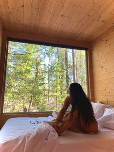 a woman sitting on top of a bed in a room with wood walls and windows