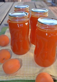 four jars filled with orange juice sitting on top of a table next to some peaches