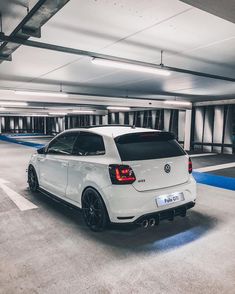 the rear end of a white car parked in a parking garage with blue lines on the floor