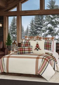 a bed with plaid comforter and pillows in front of a window overlooking the snow covered trees