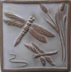 a ceramic tile with dragonflys and flowers on it's side, in the shape of a square