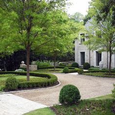 a stone house surrounded by lush green trees and shrubbery on either side of the driveway