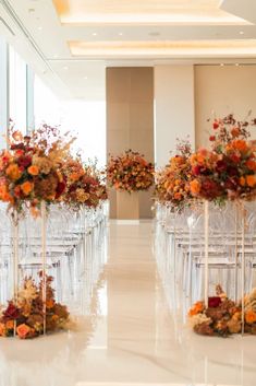 rows of clear chairs with flowers and candles on them in the middle of a hall