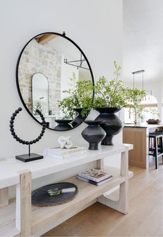 a white table topped with black vases filled with plants next to a round mirror