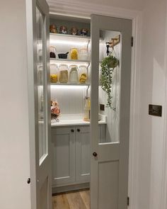 an open door leading into a kitchen with white cupboards and shelves on either side