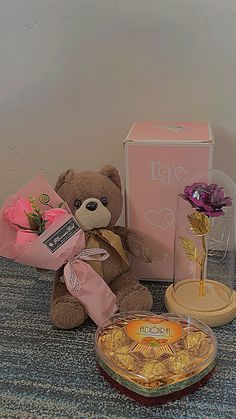 a brown teddy bear sitting on top of a table next to a box of chocolates