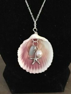 a necklace with a shell and starfish on it's side, sitting on a black stand