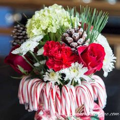 a vase filled with candy canes, carnations and pine cones on top of a table