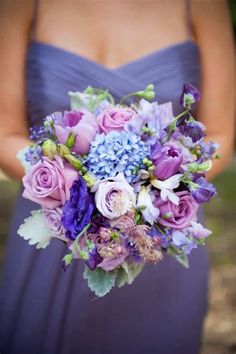 a bridesmaid holding a bouquet of purple and blue flowers in her hand,