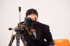 a man holding a camera up to his face while sitting in front of an orange chair