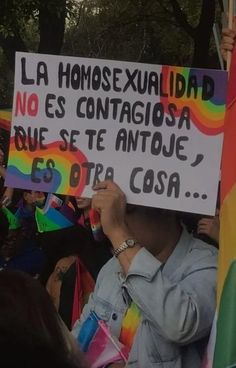 a person holding up a sign in front of a group of people with rainbow flags