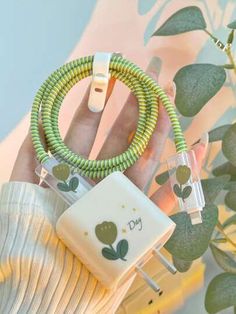 a hand holding a green and white cord with two plugs attached to it next to a plant