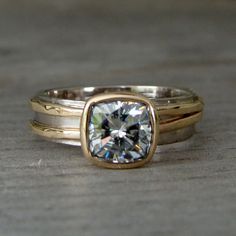 two gold wedding rings with a square cut diamond in the center on a wooden surface