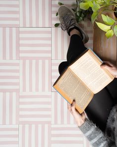 a person sitting on the floor with an open book in their lap and holding it