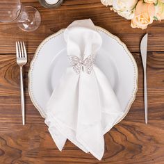 a place setting with napkins, silverware and flowers on a wooden table top