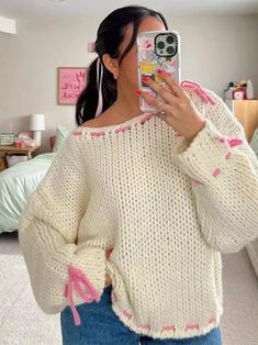 a woman taking a selfie with her cell phone in front of her face while wearing a sweater and jeans