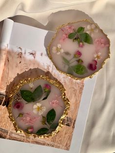 two plates with flowers and leaves on them sitting on top of a table next to an open book