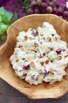 a wooden bowl filled with fruit salad next to grapes and pecans on a table