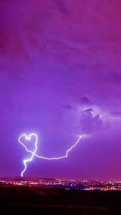 a lightning bolt is seen in the sky over a city at night with purple hues