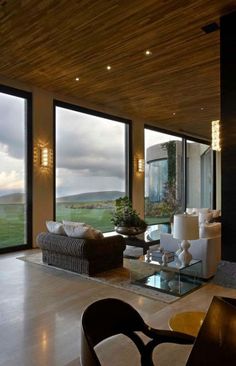 a living room filled with furniture next to large open windows and sliding glass doors that look out onto the countryside