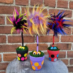 three potted plants decorated with fake grass and colorful feathers, sitting next to a brick wall