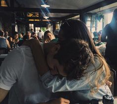 a man and woman hugging each other in front of a group of people at a restaurant