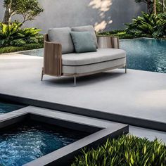 a couch sitting on top of a cement patio next to a swimming pool with plants