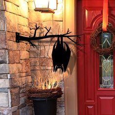 a red door with a halloween decoration hanging on it's side and a black cat in the front