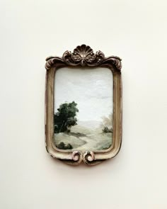 a painting hanging on the side of a white wall next to a framed object with a tree in it