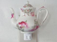 a white tea pot with pink flowers on it is plugged into a light switch