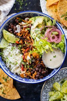 a blue and white bowl filled with rice, beans, cilantro, black beans, lettuce, red onion, avocado and tortillas