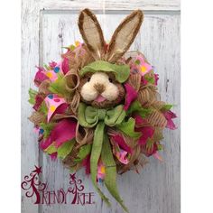 a bunny wreath hanging on the side of a white door with pink, green and yellow decorations